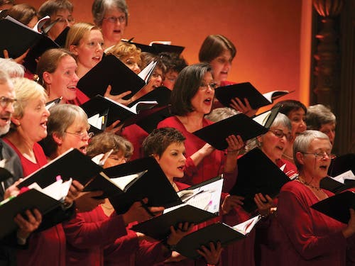 Close-up image of a choir singing on sttage, holding their music in their hands.