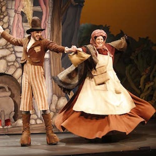 Two people on stage dressed in old-timey peasant clothing with their arms outstretched and holding hands in the middle.