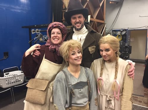 four people in costume smiling at the camera backstage. They are dressed like old-timey German peasants.