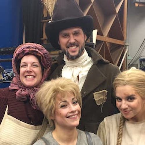 Four people in period costumes facing a camera and smiling for a candid shot in the dressing room.